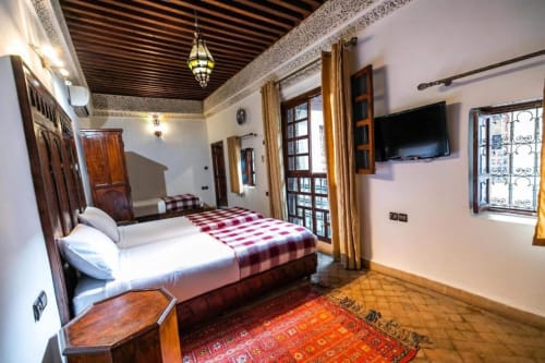 Chambre spacieuse au Riad Fes Aicha à Fès avec lit en bois traditionnel, literie écossaise rouge, plafond orné et accès à la terrasse