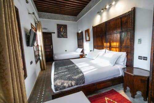 Chambre spacieuse du Riad Fes Aicha à Fès avec deux lits, mobilier traditionnel en bois, murs blancs et décor marocain