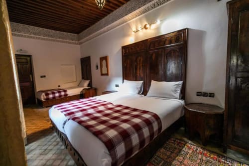 Lits jumeaux avec plaids bordeaux écossais dans une chambre spacieuse du Riad Fes Aicha à Fès, avec portes en bois sculpté