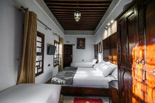 Chambre du Riad Fes Aicha avec lits multiples, portes en bois sculpté, plafond à lanterne et décor marocain traditionnel à Fès