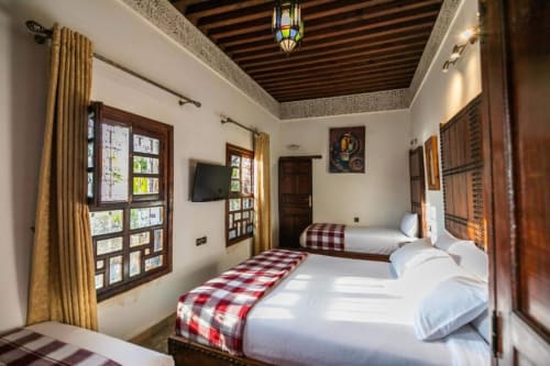 Deux lits jumeaux aux couvertures écossaises rouges dans une chambre traditionnelle du Riad Fes Aicha, Fès, Maroc