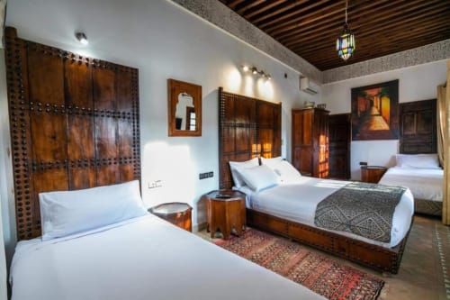 Chambre spacieuse au Riad Fes Aicha à Fès avec portes en bois sculpté traditionnel, literie blanche et décor marocain