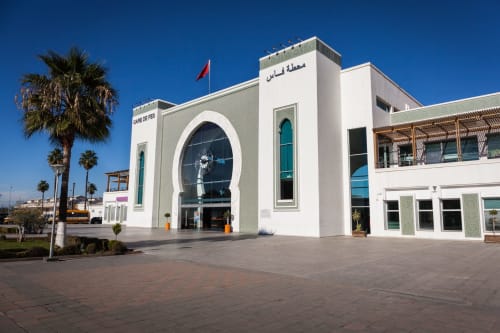 L'hôtel Le Cèdre d'Argent à Fès avec son architecture blanche moderne, palmiers et drapeau marocain sous ciel bleu