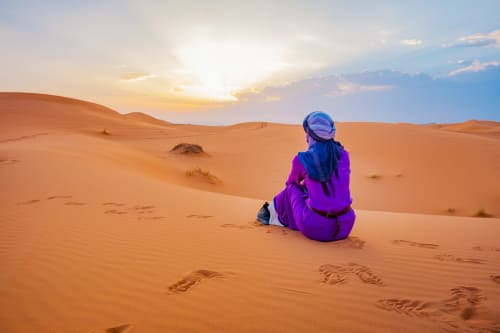 Voyageur en veste violette assis dans le désert du Sahara au coucher de soleil près de Le Cèdre D'argent, Fès Maroc