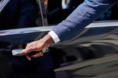 Un client ouvre la portière d'une voiture de luxe à l'hôtel Le Cèdre d'Argent à Fès, vêtu d'une veste bleue et d'un bracelet argenté