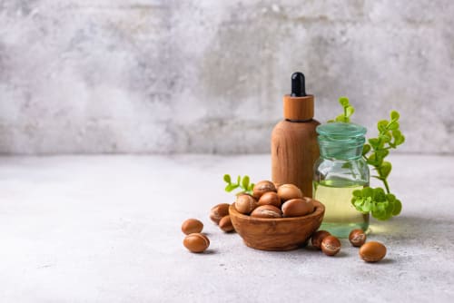 Flacon d'huile d'argan avec noix et brindilles de plantes vertes, présentant les produits de beauté naturels du Riad Fes Aicha, à Fès