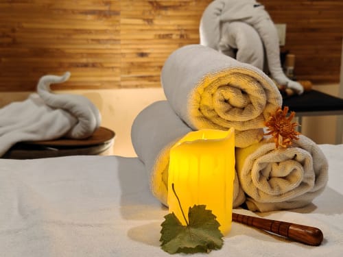 Ambiance spa et bien-être au Riad Fes Aicha : serviettes roulées, bougie jaune, fleurs et brosse en bois sur surface en bois