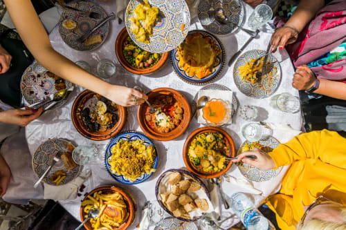 Vue aérienne de tajines marocains et plats traditionnels au Riad Fes Aicha à Fès, convives rassemblés autour.