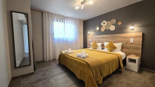 Chambre moderne au DOMAINE LANTANA Lecci avec literie moutarde, tête de lit en bois, mur d'accent foncé et assiettes décoratives tissées