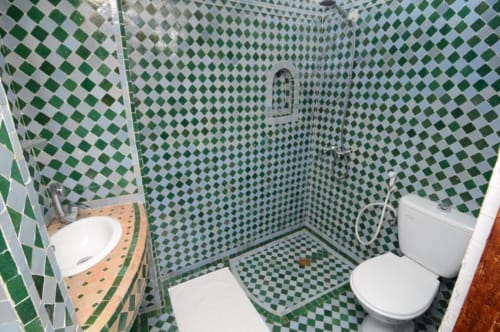 Salle de bain aux motifs losanges vert et blanc de l'hôtel Le Cèdre D'argent à Fès, équipée d'un lavabo, toilettes et douche