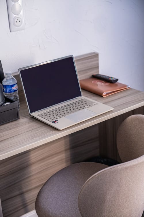 Espace de travail moderne à la Suite du Levant avec ordinateur portable argenté sur un bureau en bois, bouteille d'eau, carnet de cuir et télécommande