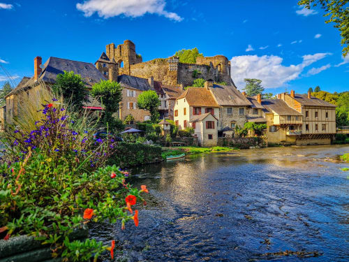 Ruines de château médiéval et maisons en pierre au bord de la rivière à Châlus, France avec fleurs colorées et ciel bleu