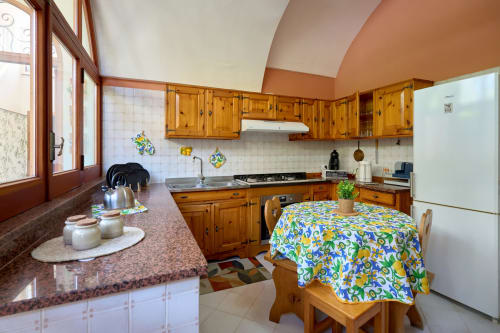 Bright kitchen with wooden cabinets, dining table with colorful tablecloth, and garden view at Sorrento Sea View villa