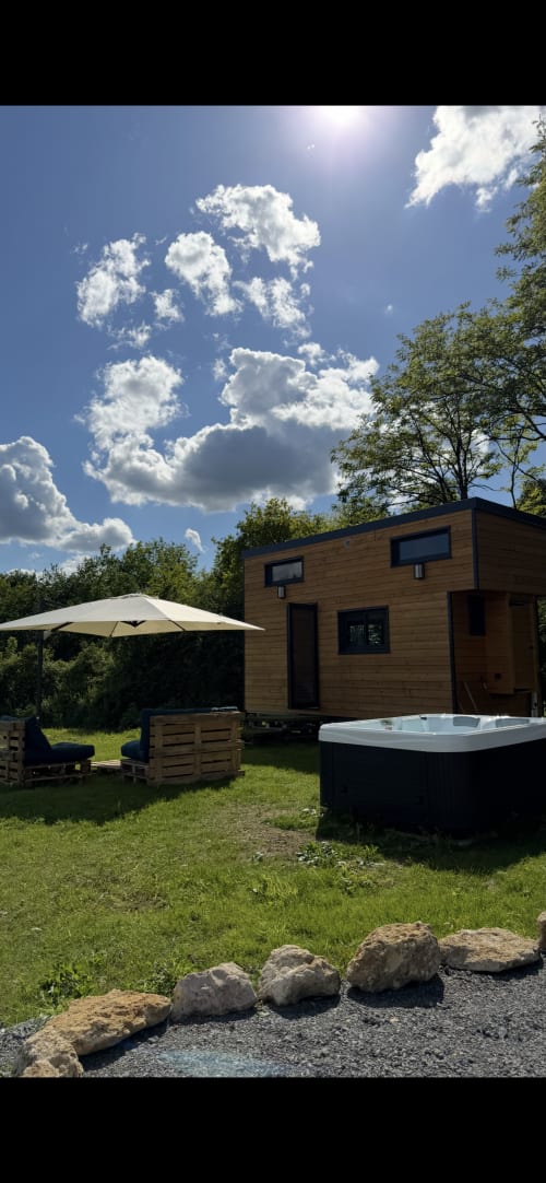 Petite maison en bois moderne à Foudre Insolite avec bain à remous, jardin détente et parasol sous ciel bleu