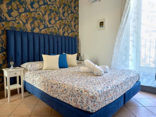 Luxury bedroom with blue upholstered headboard, floral bedding, and garden view at Sorrento Sea View villa