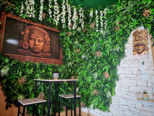 Mur végétal luxuriant orné de fleurs blanches suspendues et de masques mayas à L'expérience Love Room La Maya, L'Etrat