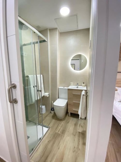 Baño moderno en Grampy Boutique Hostal con ducha abierta, inodoro, lavamanos y espejo iluminado