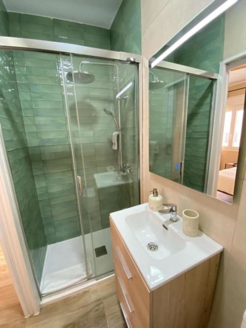 Baño moderno con ducha de azulejos verdes, lavabo blanco y espejo en Grampy Boutique Hostal, España