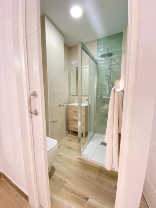 Baño moderno del Grampy Boutique Hostal con cabina de ducha de vidrio, tocador de madera y piso de madera clara