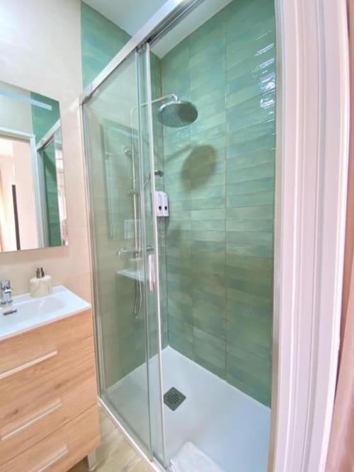 Baño privado moderno con ducha de azulejos verdes, mampara de cristal y tocador de madera en Grampy Boutique Hostal