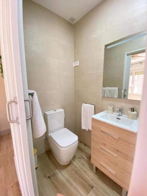 Baño moderno en habitación Grampy Boutique Hostal Superior con inodoro, tocador de madera, espejo y paredes con azulejos neutros
