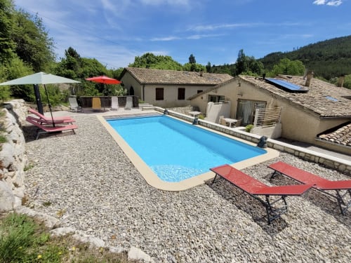 Piscine ensoleillée du gîte Domaine de la Méouge avec transats, parasols et vue sur les montagnes à Barret-sur-Méouge