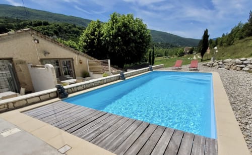 Piscine bleu cristal avec terrasse en bois, vue sur les montagnes et transats à Barret-sur-Méouge
