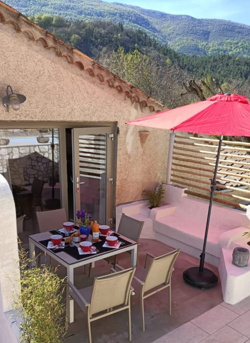 Terrasse du gîte avec table à manger, parasol rose et vue sur les montagnes au Domaine de la Méouge