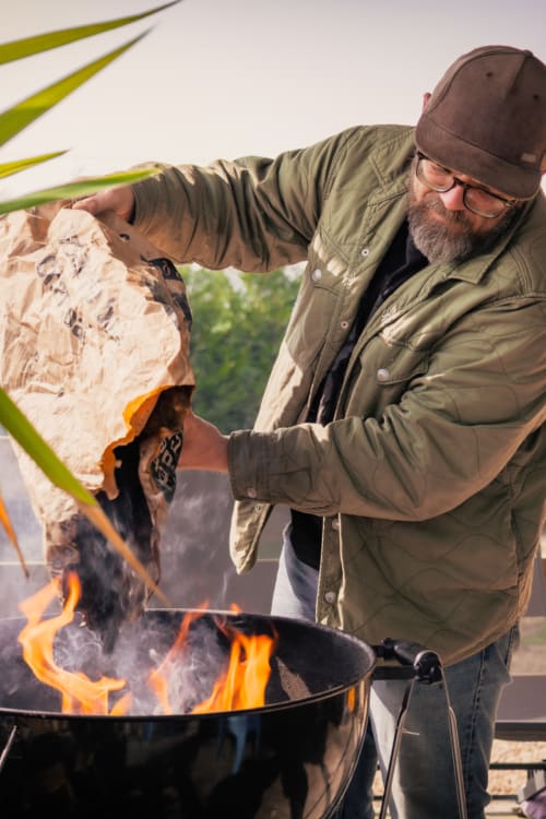Homme barbu cuisinant au feu de bois, tenant du pain frais au-dessus des flammes aux Rives du bel air, retraite rurale française