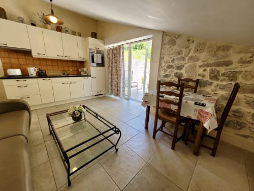 Cuisine ouverte et salle à manger du gîte de la Méouge avec meubles crème, chaises en bois, murs en pierre et accès au jardin