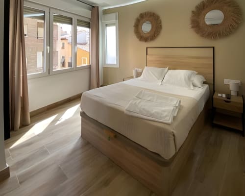 Habitación moderna y luminosa en Grampy Boutique Hostal con cama matrimonial, cabecera de madera, paredes beige, espejos decorativos y