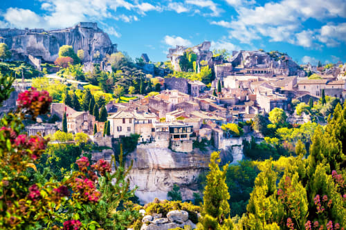Village pittoresque d'Avignon perché sur les falaises avec architecture historique, cyprès et fleurs rouges