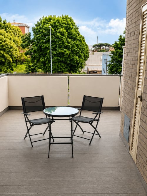 Area relax sul balcone dell'appartamento Myob a Roma con due sedie nere, tavolo rotondo e vista sulla città circondata da alberi verdeggianti