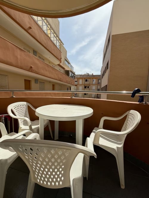 Zona de estar en balcón con sillas de plástico blancas y mesa redonda en apartamento de Fuengirola, vista de la ciudad