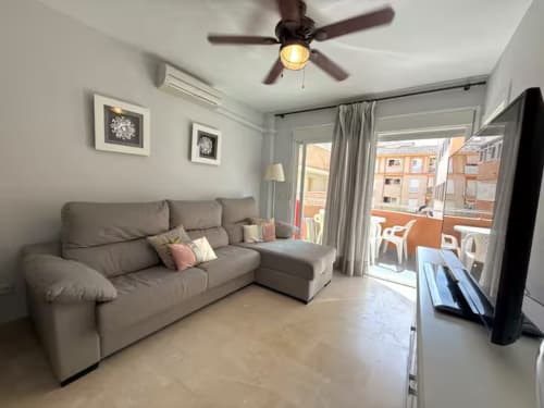 Acogedor salón de apartamento en Fuengirola con sofá gris, ventilador de techo, acceso a balcón y vistas a la ciudad