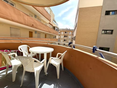 Soleado balcón de apartamento en Fuengirola con mobiliario blanco, mesa redonda y vistas de la ciudad