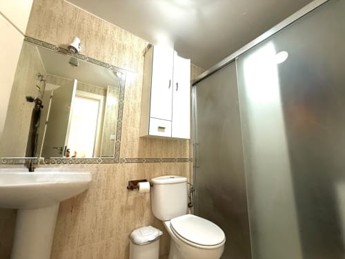 Baño moderno con lavamanos blanco, inodoro y bidé en apartamento de Fuengirola, cabina de ducha con cristal esmerilado, paredes alicatadas en beige