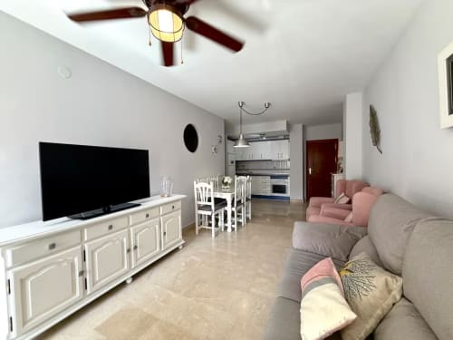 Moderno salón en Fuengirola con sofá beige, TV, comedor y cocina abierta