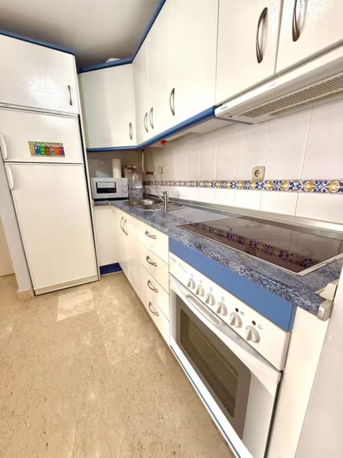 Cocina moderna en apartamento de Fuengirola con muebles blancos, detalles azules, estufa, microondas y encimeras de granito