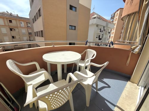 Soleada zona de estar en balcón con muebles blancos y mesa redonda con vistas al edificio de apartamentos de Fuengirola