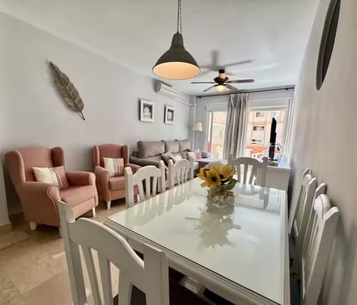 Comedor moderno con mesa blanca, sillas rosa y lámpara colgante negra en apartamento de Fuengirola