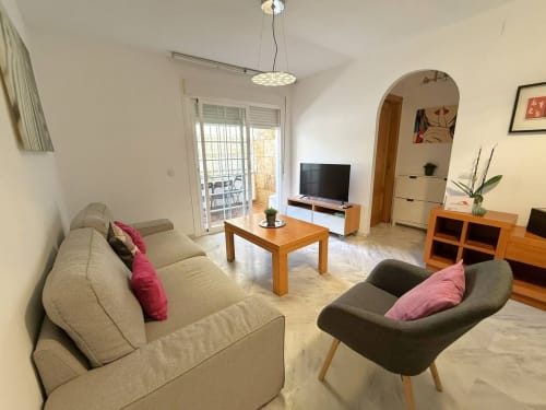 Sala de estar moderna de apartamento frente al mar en Fuengirola con asientos cómodos, muebles de madera y acceso a balcón