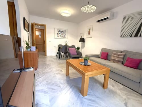 Moderno apartamento frente al mar en Fuengirola con sala de estar, mesa de madera, sofá gris, comedor y vistas a la ciudad