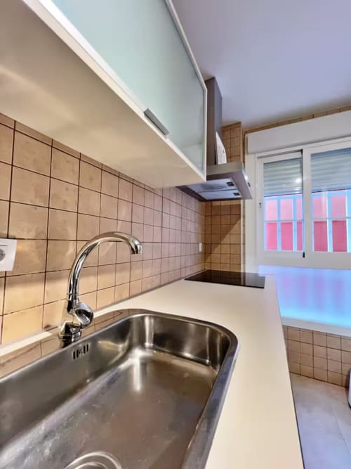 Cocina moderna con fregadero de acero inoxidable, azulejos beige y encimeras blancas en apartamento frente al mar en Fuengirola