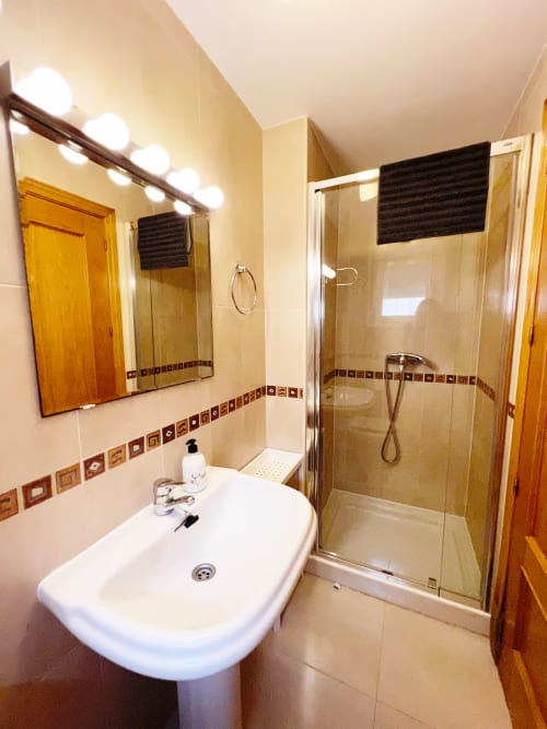Baño moderno con lavabo pedestal, cabina de ducha cristal y cenefa de azulejos decorativos en apartamento de Fuengirola