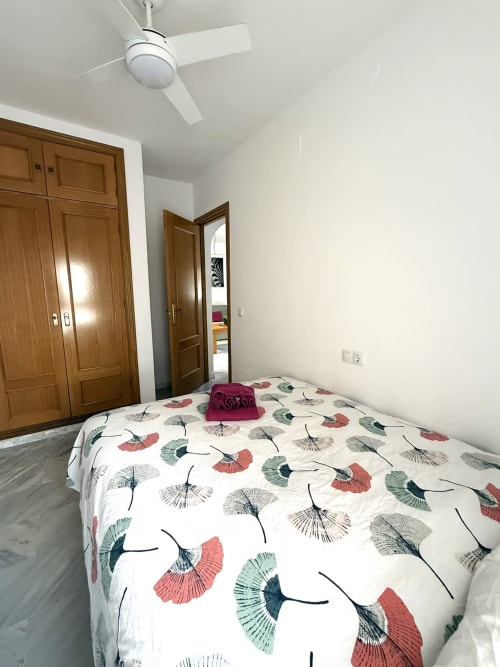 Dormitorio luminoso con ropa de cama estampada floral y armario de madera en apartamento frente al mar en Fuengirola