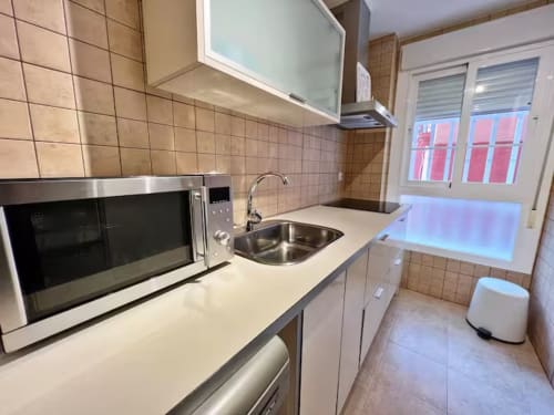 Cocina moderna con electrodomésticos de acero inoxidable, encimeras blancas y vistas a la ciudad en apartamento frente al mar, Fuengirola