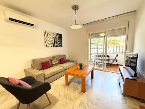 Luminoso salón en Fuengirola con sofá beige, mesa de madera y acceso a balcón con vistas al mar