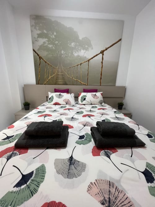 Moderno dormitorio con ropa de cama floral, toallas negras y obra de puente colgante en apartamento de Fuengirola