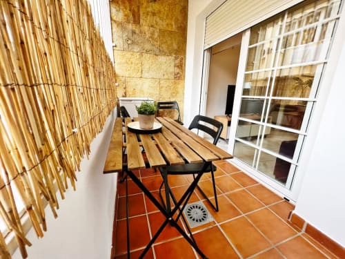 Balcón de apartamento frente al mar en Fuengirola con mesa de madera, sillas negras, azulejos de barro y vistas a la ciudad